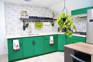 Cozinha com armários verdes, bancada branca e planta pendente.