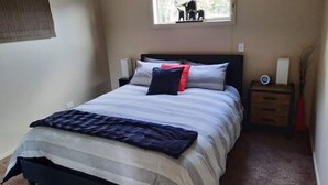 A neatly made bed with a striped bedspread, a pillow, and a bedside table with a lamp and a small clock. - Executive hideaway<br> (Christchurch)