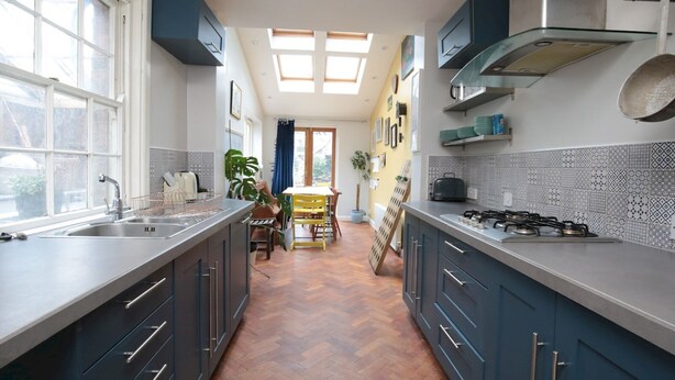 Una cucina moderna con mobili scuri, un'ampia finestra e un pavimento in legno a spina di pesce.