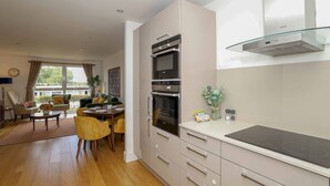 A modern kitchen with stainless steel appliances, a glass backsplash, and a dining area with yellow chairs and a table. - Stylish comfortable apartment in central Kingston - Pass the Keys (Kingston-upon-Thames)