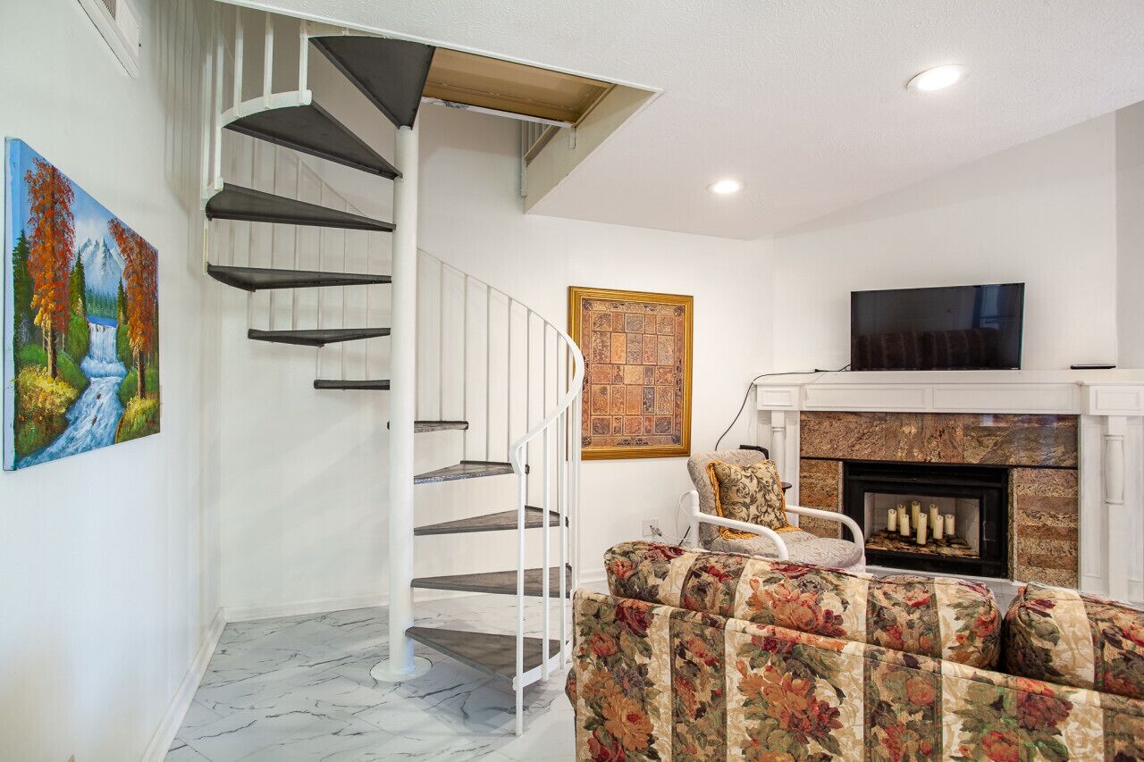 Una sala de estar moderna con una escalera espiral, una chimenea y un televisor de pantalla plana.