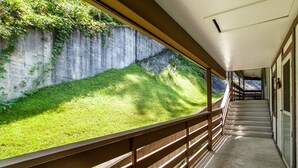 A covered walkway with a concrete wall and greenery on one side, and a staircase leading to an upper level. - Private Balcony with Scenic Views | Pool & Cozy Fireplace (Gatlinburg)