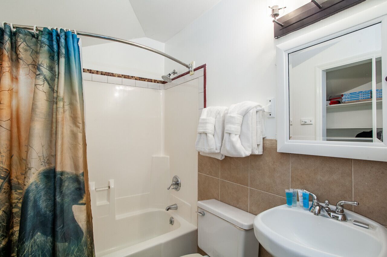 Un bagno con vasca, water e lavabo. C’è una tenda da doccia con decoro orso e asciugamani su un porta-asciugamani.