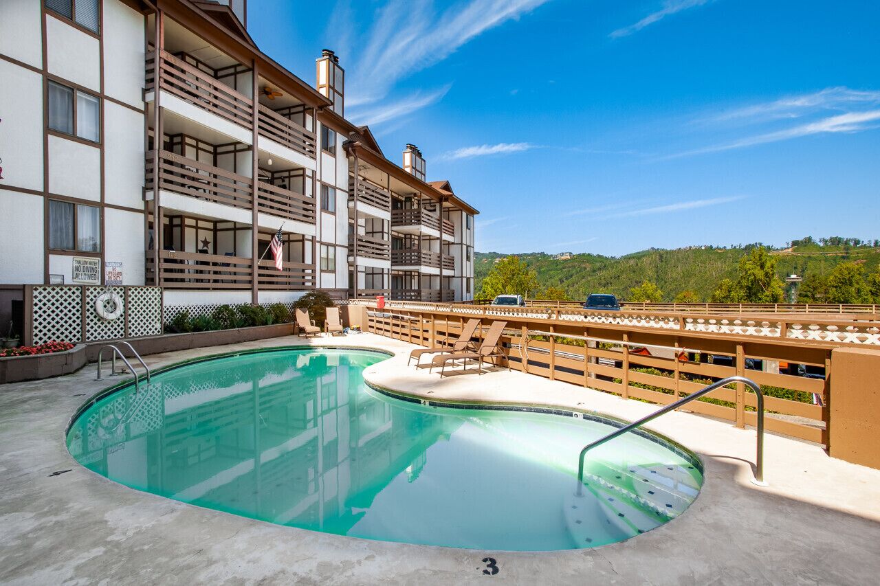 A hotel with a pool, a balcony, and a view of a hill.