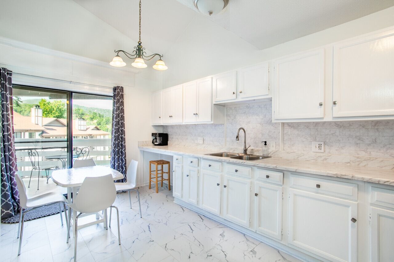 A modern kitchen with white cabinets, a marble countertop, and a dining area with a table and chairs.