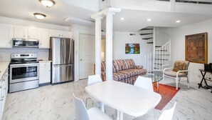 A modern kitchen with stainless steel appliances, a dining area with a white table and chairs, and a staircase leading to an upper level. - Private Balcony with Scenic Views | Pool & Cozy Fireplace (Gatlinburg)