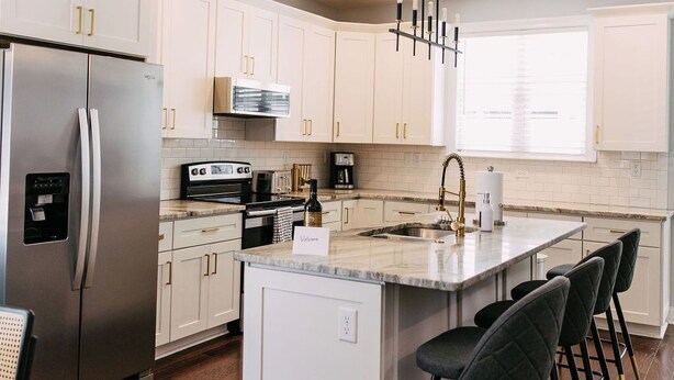 A modern kitchen with white cabinets, a stainless steel refrigerator, a built-in oven, and a central island with bar stools. - All Shook Up at Pettigrew Adventures (Memphis)