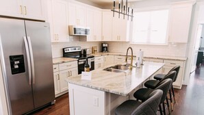 A modern kitchen with white cabinetry, a stainless steel refrigerator, a built-in oven, a sink, and a marble island with bar stools. - All Shook Up at Pettigrew Adventures (Memphis)