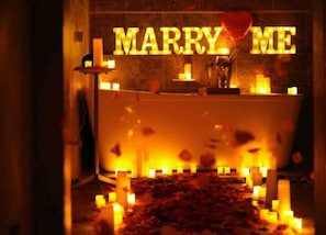 Una habitación con una bañera, velas y un letrero que dice "MARRY ME".