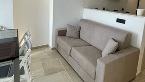 A modern living room with a sofa, a dining table, and chairs. There is a kitchen area with a stove and a range hood. The room has an arched ceiling and a tiled floor. - Greta's suite & private spa (Perinaldo)