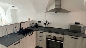 A modern kitchen with a black countertop, wooden cabinets, a built-in oven, and a microwave. - Greta's suite & private spa (Perinaldo)