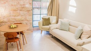 Una sala de estar con pared de piedra, un sofá blanco, una mesa redonda con sillas y una ventana con vistas.
