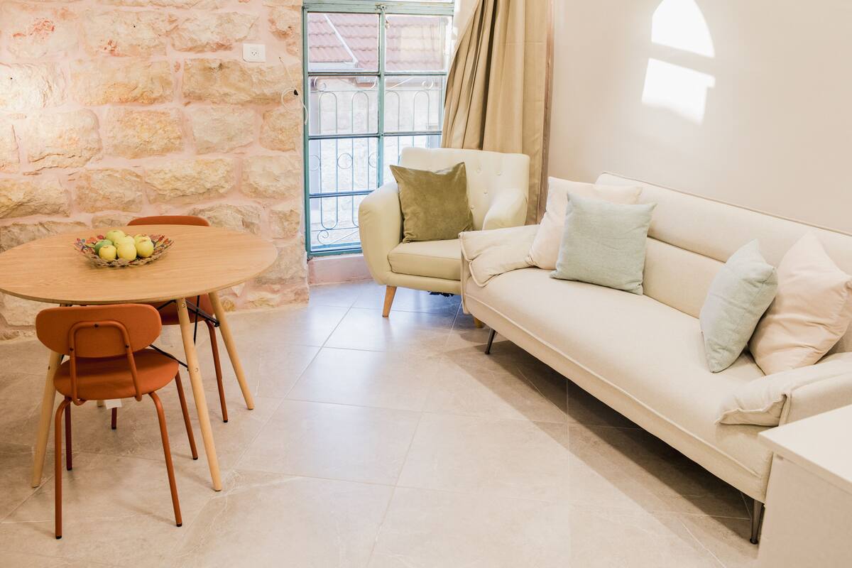 Una sala de estar con pared de piedra, un sofá blanco, una mesa redonda con sillas y una ventana con vistas.