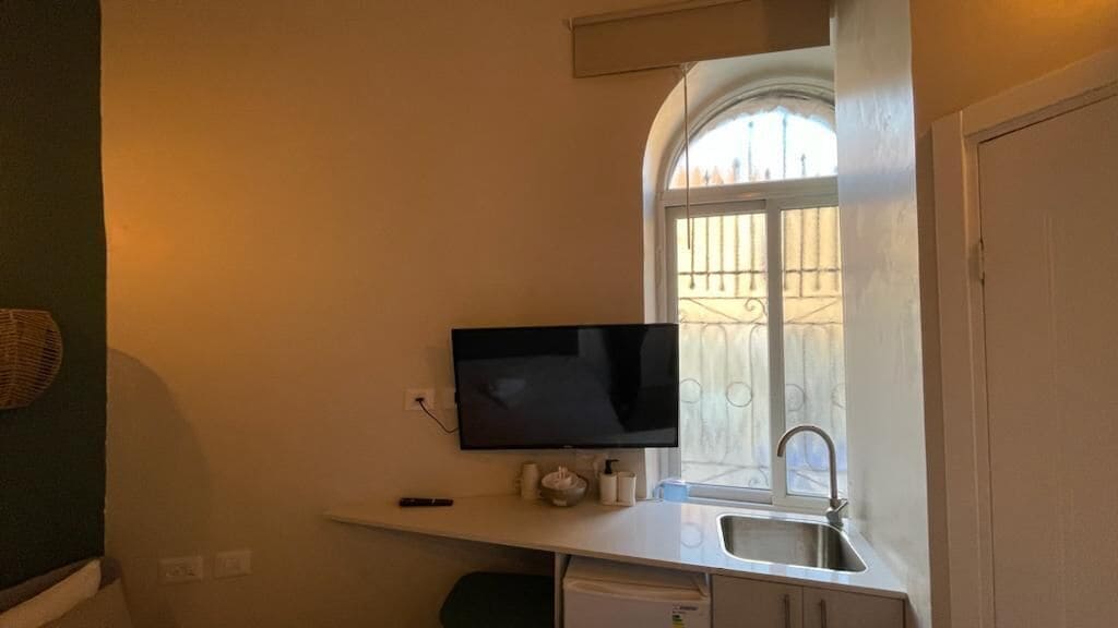 Eine kompakte Küche mit integriertem Fernseher, einem Fenster mit Metallgitter und einem Spülbecken.