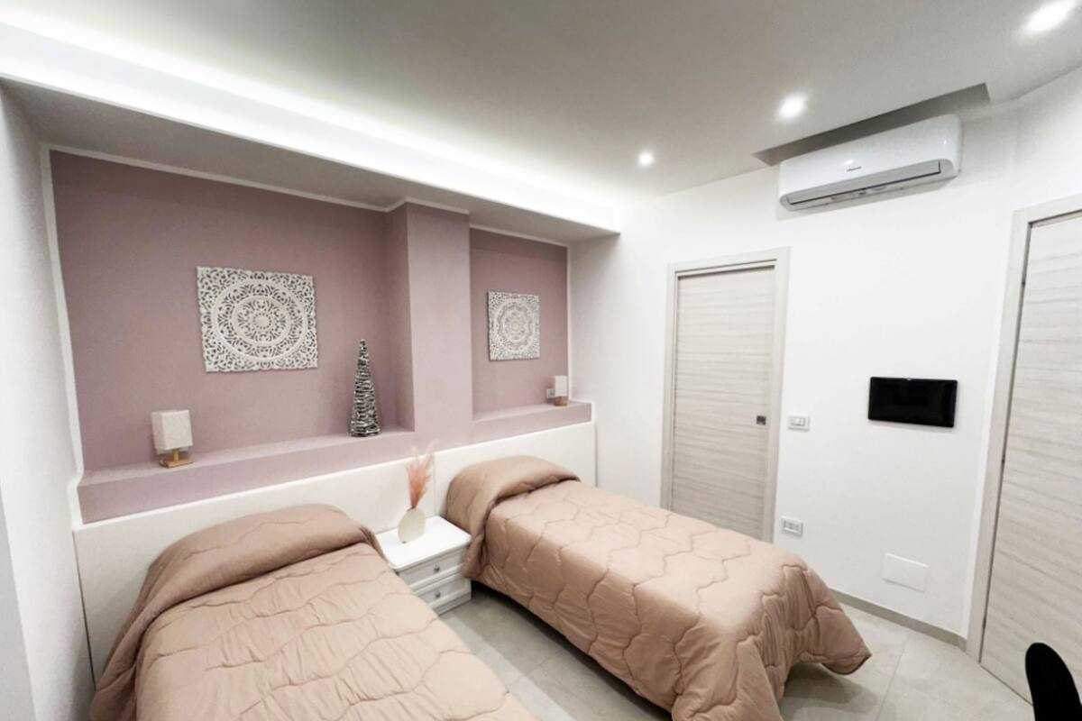 Une chambre moderne avec deux lits, une coiffeuse avec un miroir, des éléments décoratifs muraux et un système de climatisation intégré.
