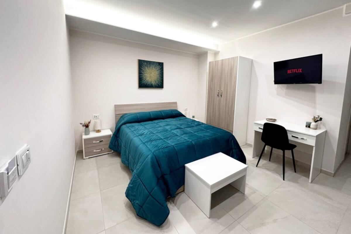 Une chambre à coucher moderne, équipée d’un lit, d’un bureau, d’une chaise, d’une armoire et d’un téléviseur fixé au mur.