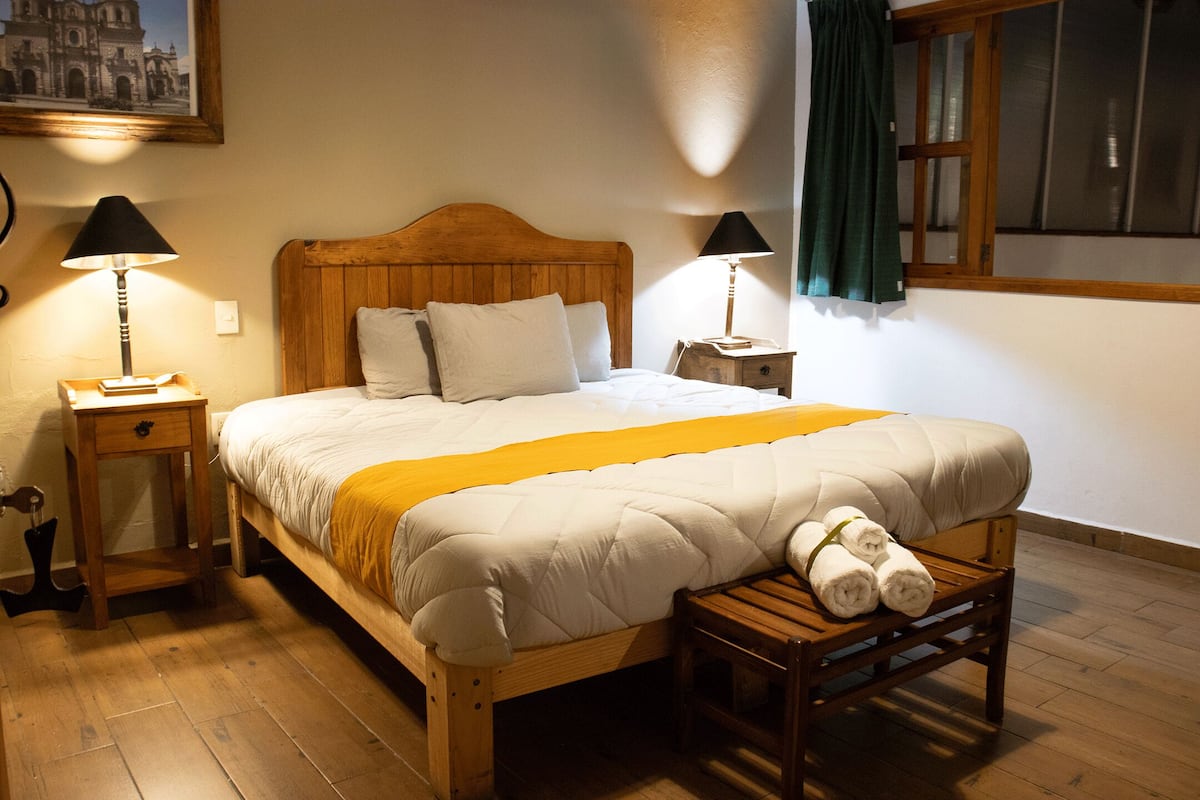 A neatly made bed with a wooden headboard, two bedside tables with lamps, and a window with curtains.