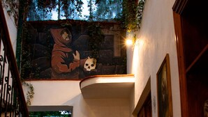 A staircase with a railing, a stone wall, and a mural of a hooded figure with a skull. - Hotel Casa del Fraile (Morelia)