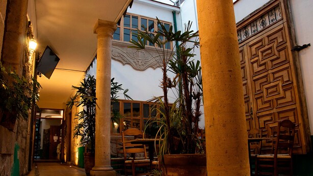 A corridor with columns, potted plants, and wooden furniture. - Hotel Casa del Fraile (Morelia)