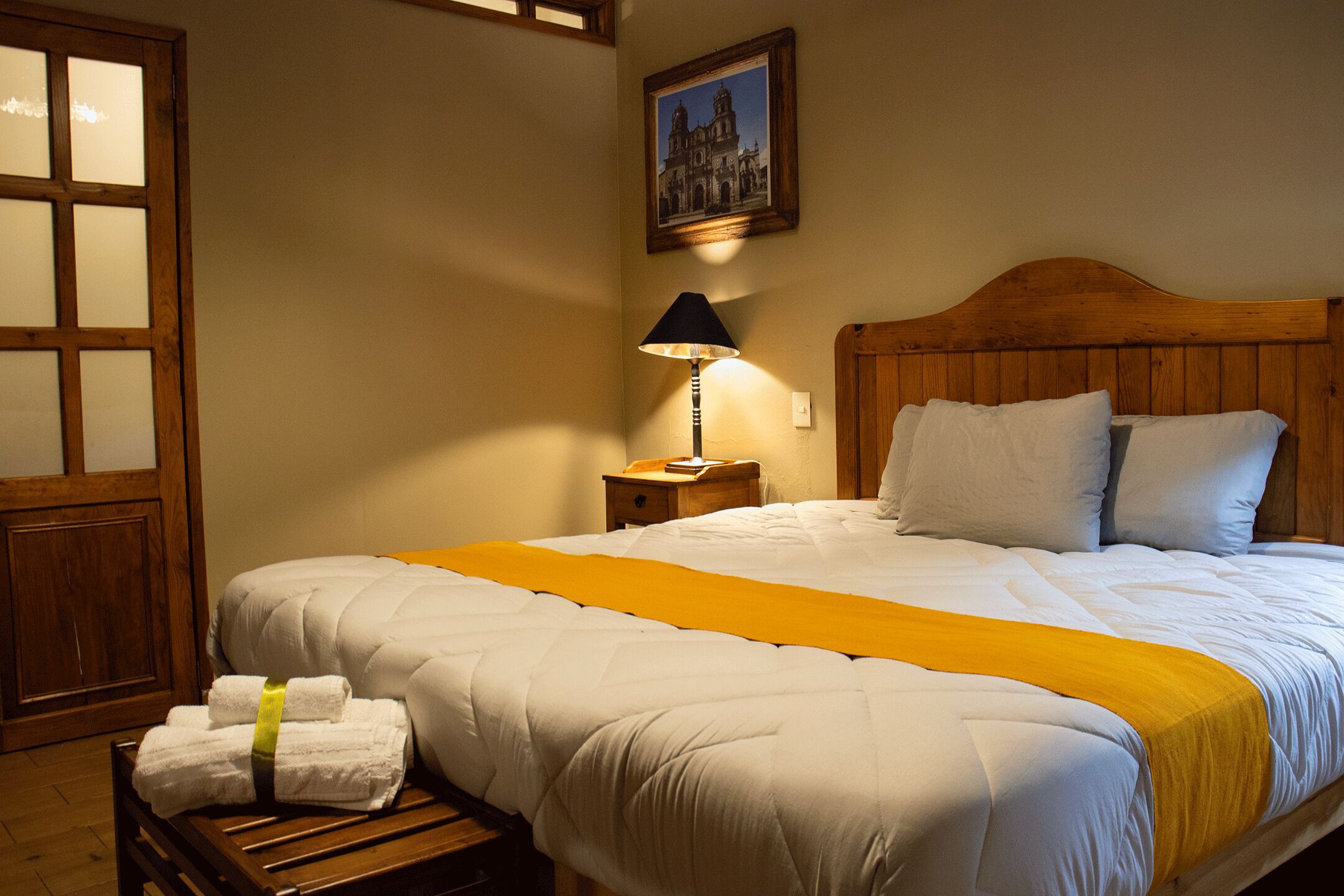 A neatly made bed with a wooden headboard, a bedside lamp, and a yellow throw blanket.