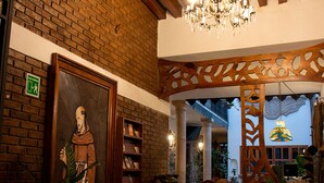 A hallway with a brick wall, wooden ceiling beams, a chandelier, and potted plants. - Hotel Casa del Fraile (Morelia)