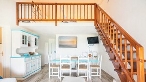 A spacious living area with a dining table, white chairs, a wooden staircase, and a view of the outside.