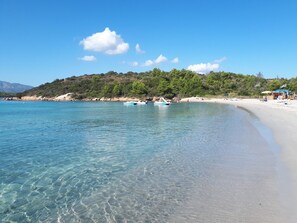 Une plage à l’eau claire, avec des bateaux et une colline boisée.