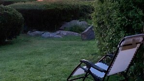 A garden with a lawn, a stone structure, and a chair. - Cala Paradiso Apt "Casa Agave" ⭐⭐⭐⭐ Sea View, Garden, WiFi, AC (Salina Bamba)