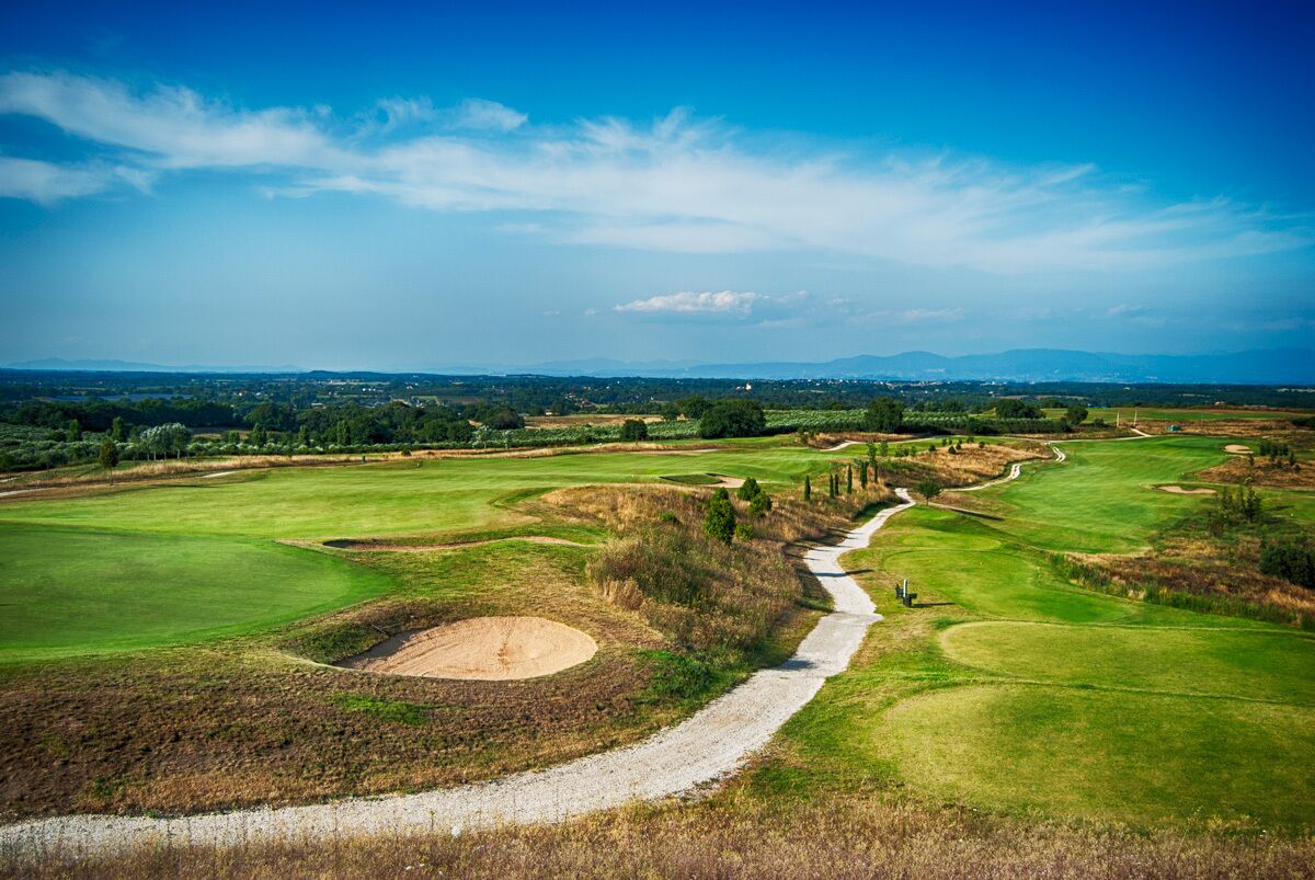 Un campo de golf con un sendero sinuoso, búnkeres de arena y montañas a lo lejos.