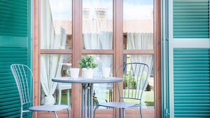 Une petite terrasse avec une table ronde et deux chaises, un pot de fleurs et une fenêtre avec des rideaux.