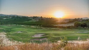 Un parcours de golf avec un coucher de soleil en arrière-plan, des collines ondoyantes et une végétation clairsemée.