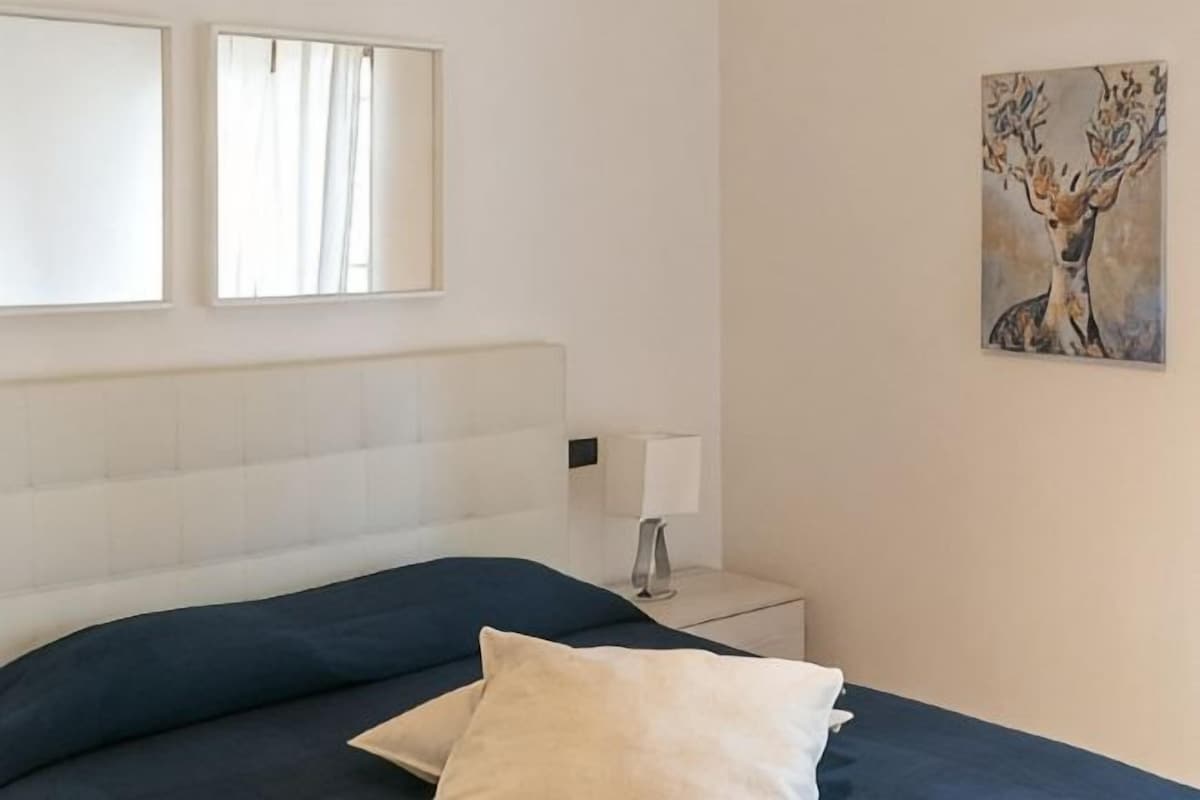 Une chambre à coucher avec un lit, une lampe de chevet et un tableau représentant un cerf.