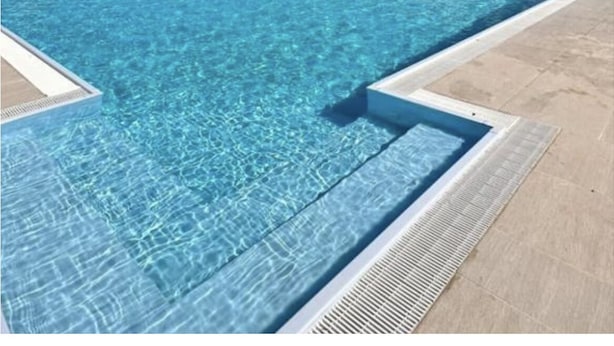 Une piscine d’eau bleue et limpide, avec vue sur un paysage vallonné et un ciel dégagé.