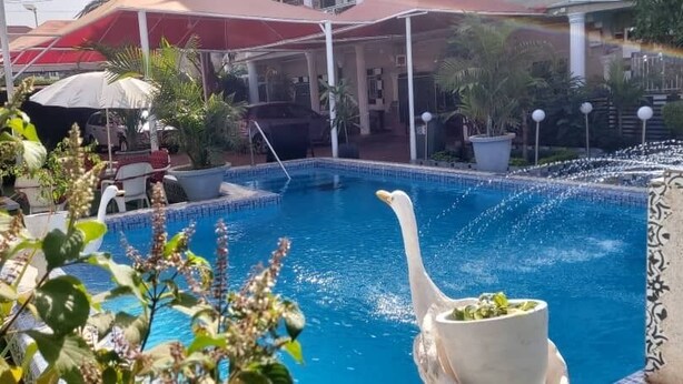 A swimming pool with a swan decoration, surrounded by potted plants and umbrellas. - Sweet Mama Residence  (Serrekunda)