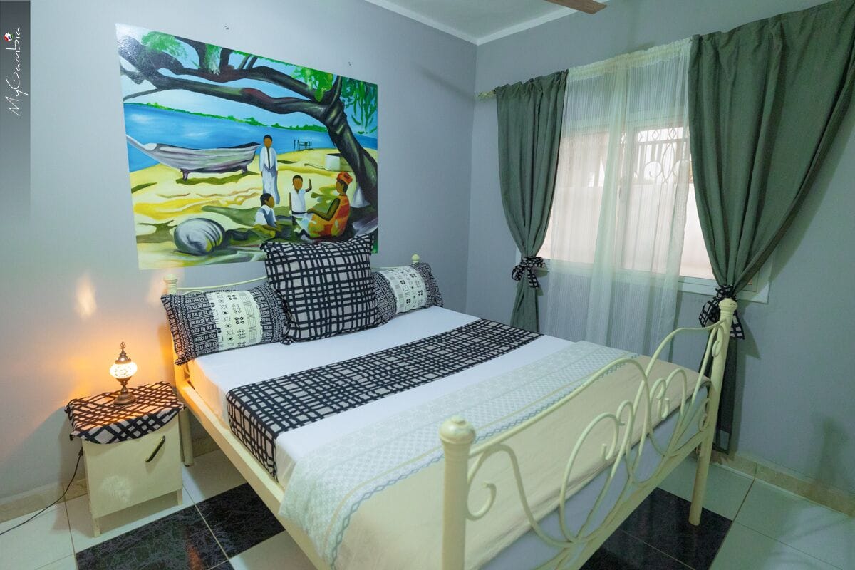 A bedroom with a bed, a nightstand, a painting, and a window with curtains.