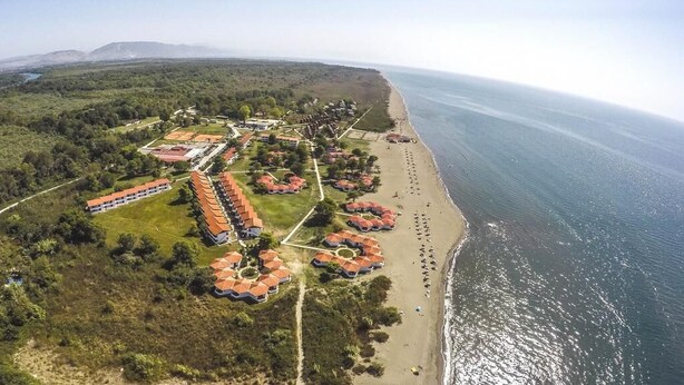An aerial view of a coastal resort with multiple bungalow-style buildings, a beach, and a clear view of the ocean. - Vila Elkom Apartment 2 (Ulcinj)