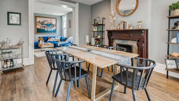 Un comedor con una mesa larga y sillas, una chimenea y una sala de estar con un sofá y obras de arte.