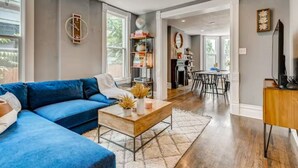 Una sala de estar moderna con un sofá seccional azul, una mesa de centro de madera y un comedor con una mesa y sillas blancas.