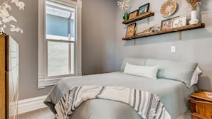 Un dormitorio con una cama grande, una ventana y estantes en la pared con objetos decorativos.