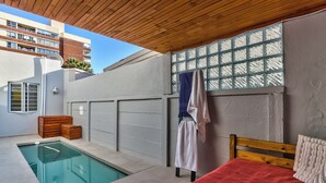 A bedroom with a wooden headboard, a bed with a red blanket, a small pool, and a window with a view of a building.