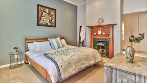 A bedroom with a bed, a fireplace, a vase with flowers, and a small table.