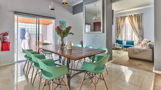 A dining area with a wooden table and green chairs, a vase with flowers, and a large mirror on the wall.