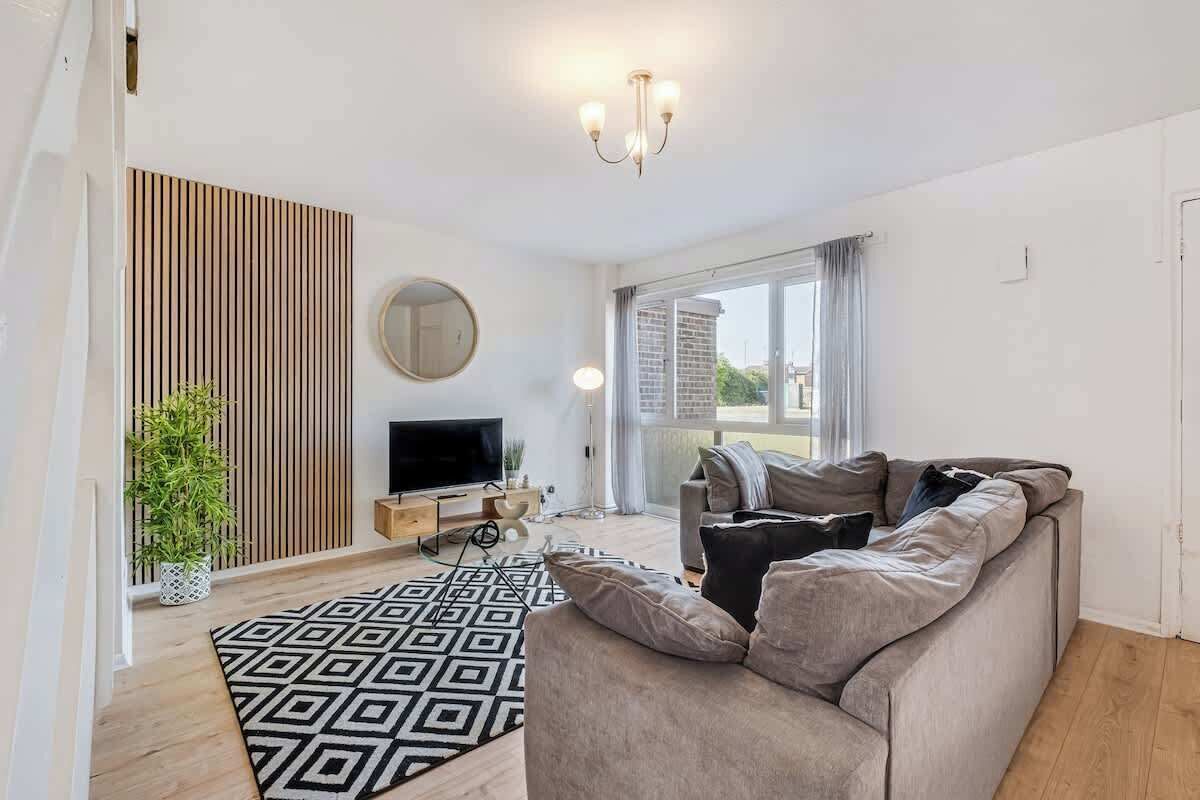 Ein modernes Wohnzimmer mit einer Couch, einem Fernseher, einem gemusterten Teppich und einem großen Fenster.