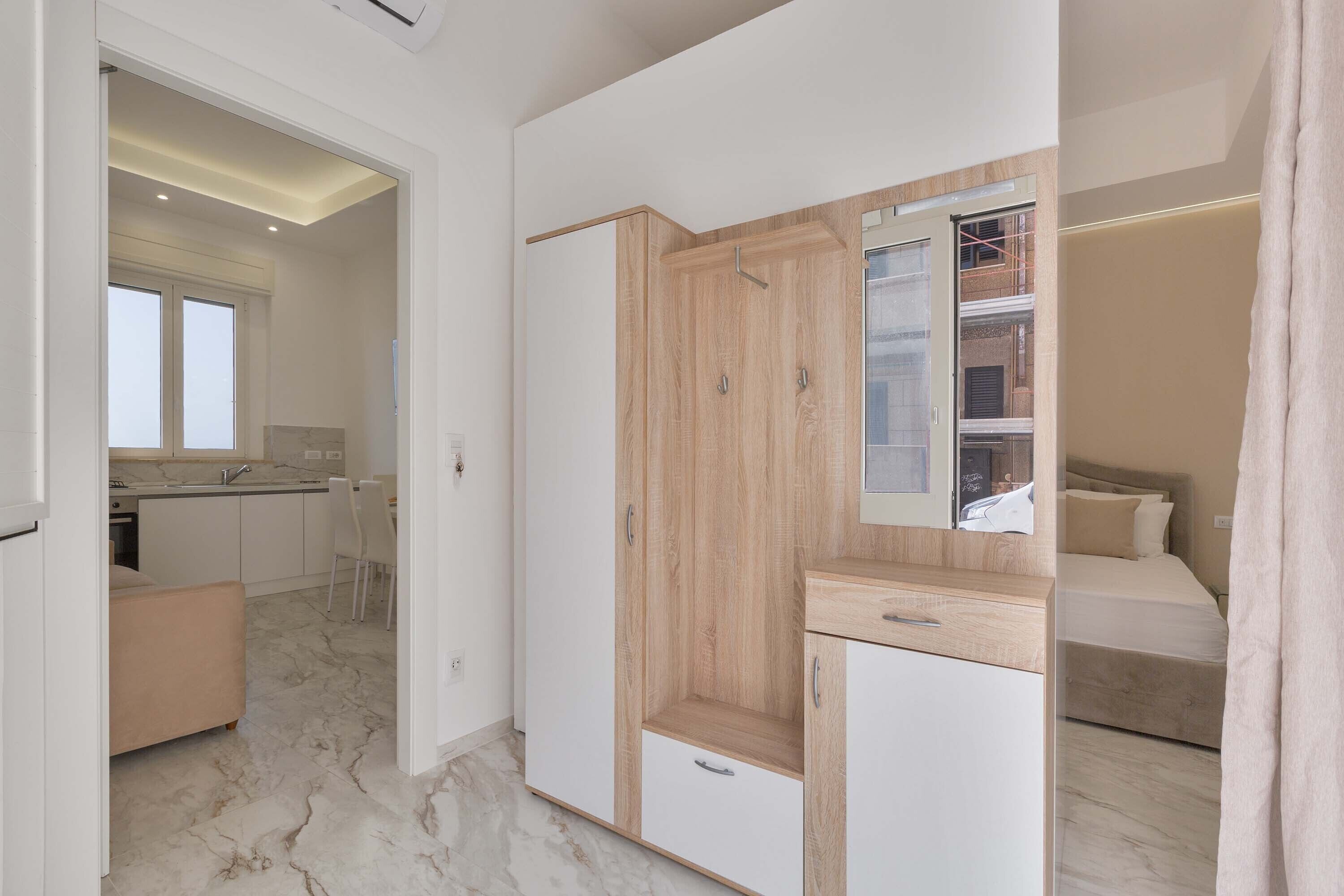 A modern bedroom with a bed, a wooden wardrobe, a small desk, and a bathroom visible through an open door.