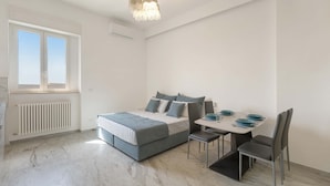 Ein modernes Schlafzimmer mit einem großen Bett, einem Esstisch mit Stühlen und einem Fenster mit Jalousien.