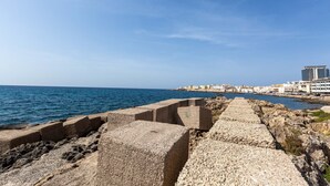 Eine Küstenpromenade mit freiem Blick auf das Meer und einer entfernten Stadtlandschaft.