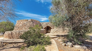 A stone building with a central arched doorway, surrounded by vegetation and a stone pathway. - 3621 Tenuta Terra del Sole by Perle di Puglia (Casarano)