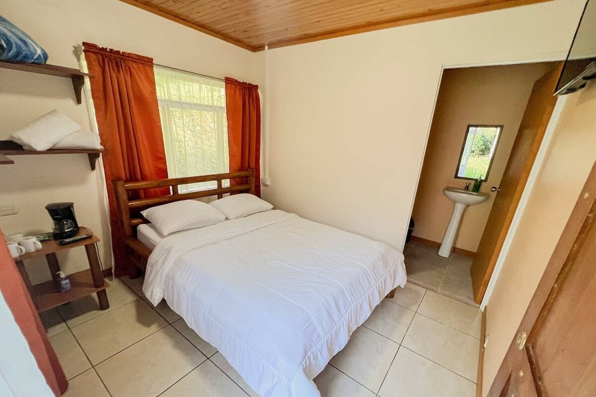 Une chambre à coucher avec un lit, une table de chevet, une machine à café et une fenêtre avec des rideaux.