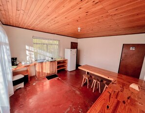 Una cocina compacta con techo de madera, un refrigerador, un lavamanos y una zona de comedor con taburetes.