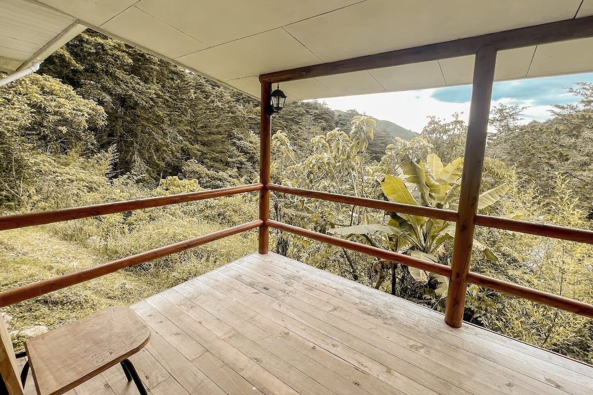 Une terrasse en bois avec une rambarde en métal, offrant une vue sur un paysage verdoyant et vallonné.